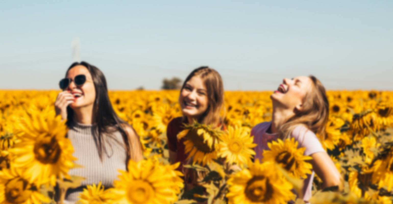 A small blurry photo of three women sanding on a sunflower field